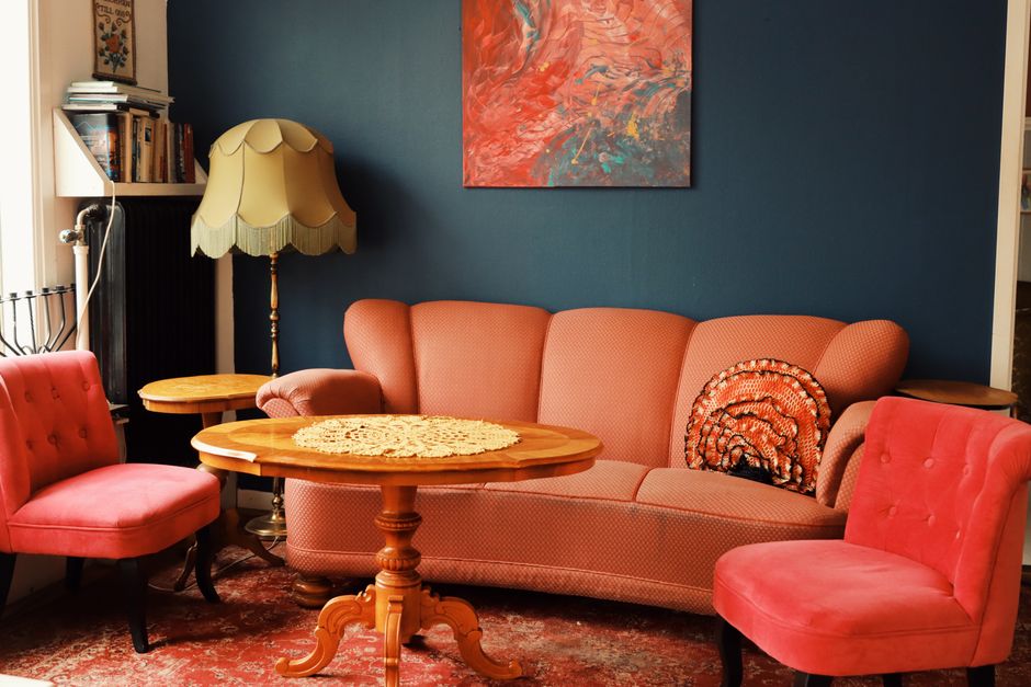 Close-up of a vintage patterned upholstered sofa with a red and beige Persian-style rug on the armrest, illuminated by warm natural light. A white lace doily partially covers the top of the sofa, which appears clean and well-maintained, highlighting the intricate design and vibrant colors of the textiles. The setting suggests a cozy, traditionally decorated living room, emphasizing surface cleaning and upholstery care. Barnes Carpet Cleaning specializes in deep cleaning and sanitisation for domestic furniture, ensuring hygiene and preservation of delicate materials. The scene reflects careful surface maintenance typical of professional cleaning services offered by Barnes Carpet Cleaning, as shown on the page about Lonsdale Road residents rug and upholstery cleaning tips.